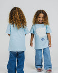Two children (twins) wearing matching light blue t-shirts and jeans on a white background