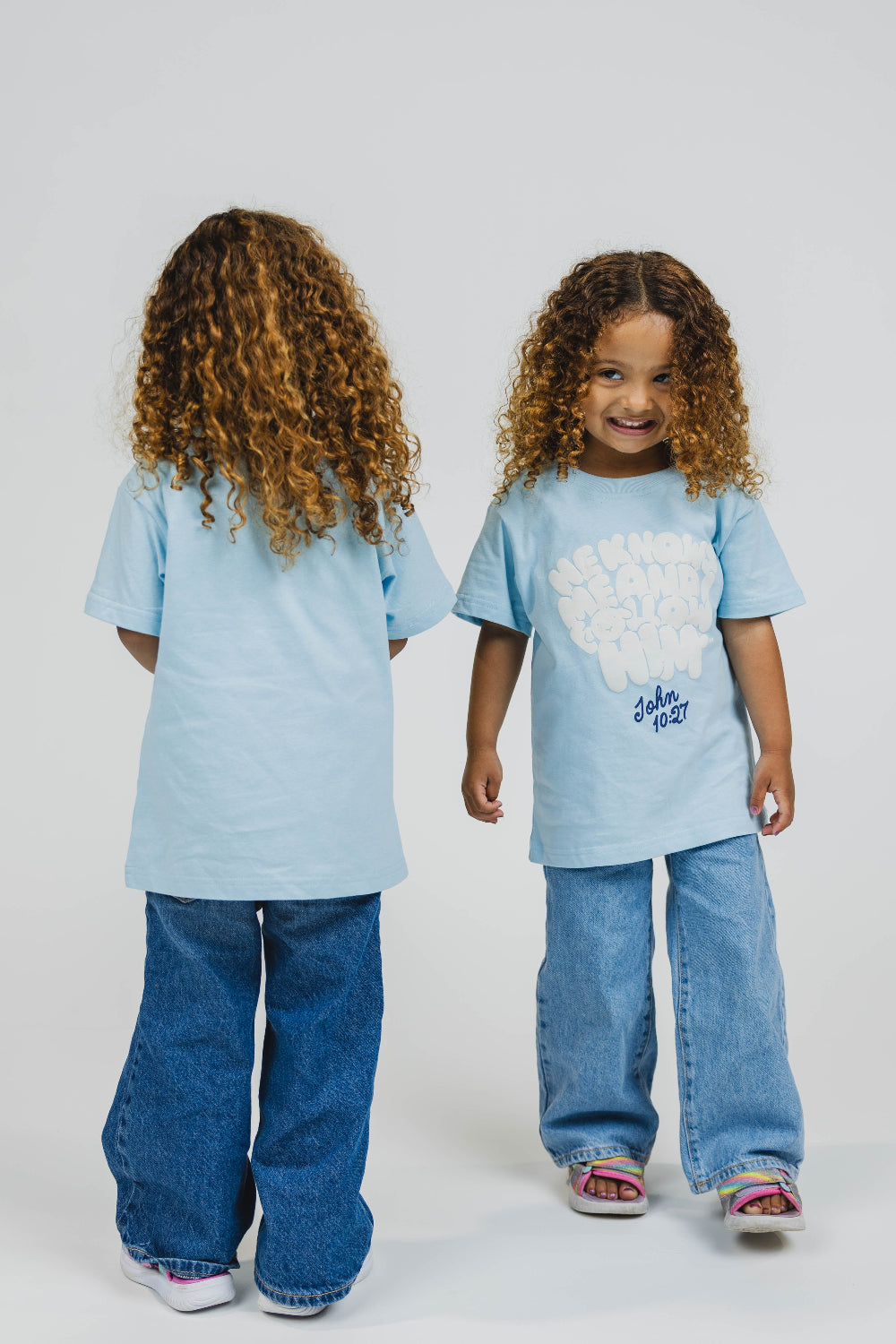 Two children (twins) wearing matching light blue t-shirts and jeans on a white background